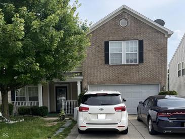 Two-story brick home featuring a front lawn, attached garage, and cars parked in the driveway at 12509 Teacup Way, Indianapolis, IN 46235