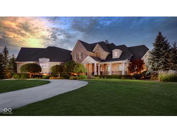 Stunning stone home with lush lawn, covered porch, and circular driveway at dusk at 13346 W Sherbern Dr, Carmel, IN 46032