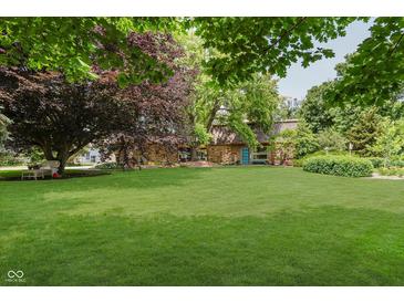 Landscaped front yard with mature trees and a stone house facade exudes a warm and inviting curb appeal at 1810 S Raceway Rd, Indianapolis, IN 46231