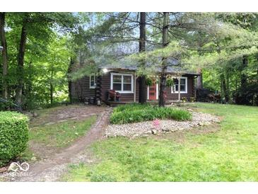 Charming log cabin with a red door surrounded by a lush green yard and mature trees at 20417 State Road 37 N, Noblesville, IN 46060