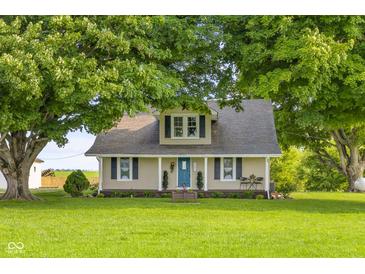 Charming tan farmhouse-style home with a covered front porch and lush green lawn and mature trees at 14855 E State Road 46, Columbus, IN 47203