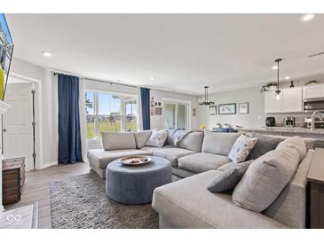 Comfortable living room with large windows, gray sectional, and open access to the kitchen at 19387 Astoria Ave, Sheridan, IN 46069