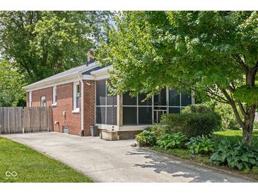 Charming brick home featuring a screened-in porch, lush landscaping, and a well-maintained lawn and a concrete driveway at 5126 Hillside Ave, Indianapolis, IN 46205
