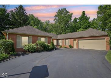 Brick house featuring an attached garage, asphalt driveway, and tasteful landscaping under a vibrant sky at 7029 Kingswood Cir, Indianapolis, IN 46256