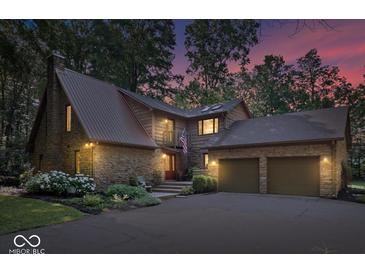 Charming stone home boasts a two-car garage, beautiful landscaping, and a welcoming entrance with an American flag at 6975 Milhouse Rd, Indianapolis, IN 46221