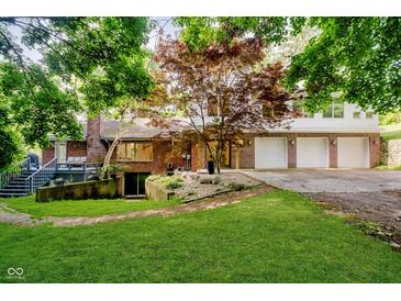 Charming brick home featuring a well-manicured lawn, mature trees, and an attached three car garage at 1065 E 76Th St, Indianapolis, IN 46240