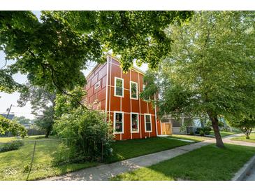 Stylish two-story home with a unique red exterior and white trim, surrounded by lush greenery and a well-manicured lawn at 1210 Churchman Ave, Indianapolis, IN 46203