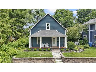 Charming blue two-story home featuring a cozy front porch with white columns and lush landscaping at 6107 Broadway St, Indianapolis, IN 46220