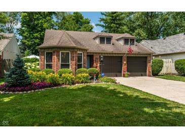 Charming brick home with an attached garage and a beautifully landscaped front yard with colorful flowers at 9520 Settlement W Dr, Indianapolis, IN 46250