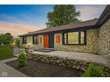 Charming stone home featuring a decorative wood door, landscaped yard, and beautiful exterior lighting at 5550 W Mooresville Rd Byp, Indianapolis, IN 46221