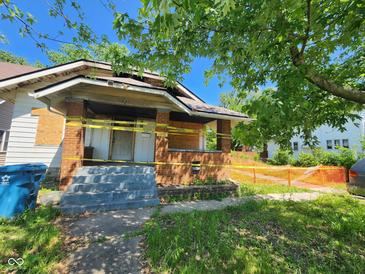 Weathered exterior with damaged porch, boarded windows, caution tape, and overgrown lawn at 1031 Blaine Ave, Indianapolis, IN 46221
