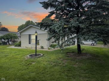 Well-maintained home featuring a green lawn, mature trees, and charming exterior lighting at dusk at 4329 Rutgers Dr # 40B, Anderson, IN 46013
