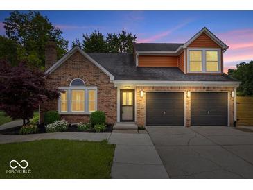 Charming brick home features a two-car garage, manicured lawn, and welcoming front entrance at dusk at 9385 Helmsdale Dr, Indianapolis, IN 46256