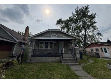 Charming stone home featuring a covered front porch and mature landscaping at 1214 Wallace Ave, Indianapolis, IN 46201