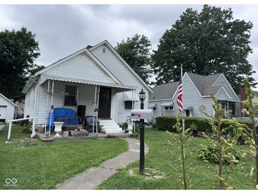 A charming single-story home with a covered porch and an American flag in a mature, tree-lined yard at 1768 N Lynhurst Dr, Speedway, IN 46224