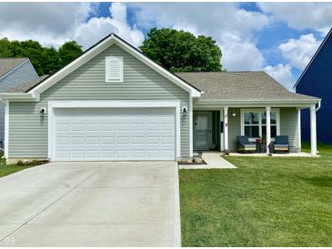 Charming single story home features a two-car garage, covered porch with chairs, and a well-manicured lawn at 213 Drewood Dr, Trafalgar, IN 46181