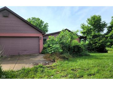 A charming house with a two-car garage is surrounded by overgrown vegetation at 6003 S 125 W, Trafalgar, IN 46181
