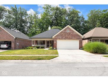 Charming brick home featuring a manicured lawn, front porch, and a two-car garage with a beautiful blue sky overhead at 9735 Woodsong Ln, Indianapolis, IN 46229