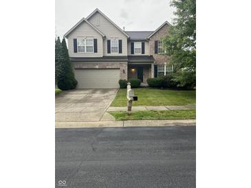 Two-story home featuring a brick and tan siding exterior, a two-car garage, and a well-manicured front yard at 14375 Leland Muse, Fishers, IN 46037