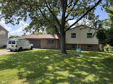 Charming split-level home featuring a brick facade, attached garage, large tree, and a swing in a grassy front yard at 3525 Valley Lake Dr, Indianapolis, IN 46227