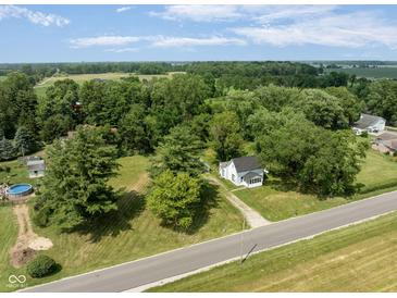 Aerial view of a quaint white home surrounded by mature trees and a vast, lush green lawn at 16000 W 700 S, Anderson, IN 46017