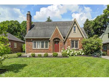 Charming brick home featuring a well-manicured lawn, flowering bushes, and a classic red door at 5430 N Kenwood Ave, Indianapolis, IN 46208