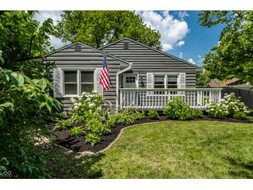 Charming gray home featuring a welcoming front porch, lush landscaping, and an American flag at 5660 Crittenden Ave, Indianapolis, IN 46220