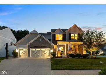 Charming two-story home with a three-car garage, manicured lawn, and inviting front porch at twilight at 12998 Silbury Hill Way, Fishers, IN 46037