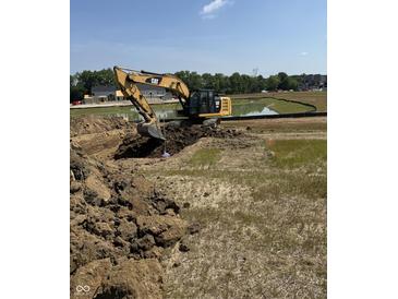 Construction site with a CAT excavator digging a trench next to a pond in preparation for new home construction at 1424 Chatham Ridge Ct, Westfield, IN 46074