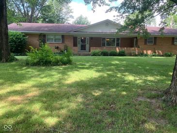 Ranch home featuring a brick facade, covered front porch, and a spacious, grassy front yard with mature trees at 106 N 300 W, Greenfield, IN 46140