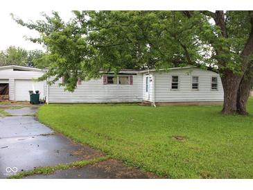 Exterior view of a home with white siding, surrounded by lush greenery and a mature tree at 220 S 2Nd St, Summitville, IN 46070