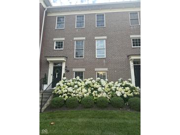 Charming brick townhome featuring a black front door, elegant trim, and lush hydrangea bushes at 12838 Bird Cage, Carmel, IN 46032
