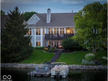 Back view of a luxurious lake house with a boat dock, lush green lawn, and mature trees at 11137 Peppermill Ln, Fishers, IN 46037