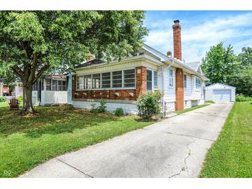 Charming home with a brick chimney, a well-manicured lawn, and a long driveway leading to a detached garage at 1411 N Linwood Ave, Indianapolis, IN 46201