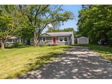 Charming single-story home with a red front door, gravel driveway, and detached garage surrounded by mature trees at 7424 North Dr, Lawrence, IN 46226