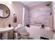 Elegant bathroom features a marble-style tile tub and shower, a pedestal sink and a modern round mirror at 5964 Laramie Trl, Columbus, IN 47203