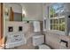 Bathroom with beige tile, sink, toilet, wall lighting, and window with shutters at 4807 Graceland Ave, Indianapolis, IN 46208