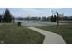 Community basketball court next to a pond with a paved walkway and green grass at 12912 Broncos Dr, Fishers, IN 46037