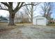 View of a detached white one car garage in backyard with gravel driveway and mature trees at 825 Arrow Ave, Anderson, IN 46016
