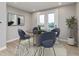 Bright dining area featuring a round glass table, blue chairs, contemporary artwork, and doors leading to a balcony at 7348 W County Road 600 Rd # 12-604, McCordsville, IN 46055