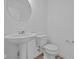 Cozy powder room with pedestal sink, round mirror, and modern fixtures at 6114 Paperbark Way, Indianapolis, IN 46259