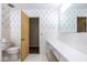 Classic white tiled bathroom with vintage wallpaper and a view into another carpeted room at 7027 Creekside Ln, Indianapolis, IN 46220