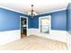 Dining room boasts modern chandelier, blue accent wall, wainscotting, and an adjacent door to the kitchen at 475 Golf Ln, Indianapolis, IN 46260