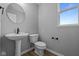 Cozy powder room showcasing a pedestal sink, a round mirror, and a toilet. A window offers natural light at 1713 Real St, Indianapolis, IN 46240