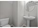 Bathroom with a pedestal sink, toilet and round mirror with modern fixtures and neutral tones at 1721 Real St, Indianapolis, IN 46240