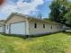 Spacious two-car garage attached to a tan home, surrounded by a lush green lawn under a bright sky at 1608 Edgecombe Ave, Indianapolis, IN 46227