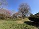 Green backyard with lush grass, mature trees, and blooming purple and pink flowers at 6628 E Michigan St, Indianapolis, IN 46219