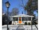 Charming single-story home featuring an orange front door and a screened in porch, complemented by snowy front yard at 5630 Winthrop Ave, Indianapolis, IN 46220