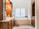 Bright bathroom featuring custom wood cabinets, soaking tub with marble surround, and a large picture window at 9399 Irishmans Run Ln, Zionsville, IN 46077