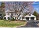 Two-story home with attached two-car garage and black asphalt driveway surrounded by landscaped lawn and mature shade tree at 128 Wellington Rd, Indianapolis, IN 46260